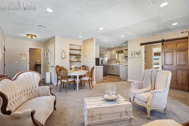 living room with light colored carpet, radiator heating unit, a barn door, and a drop ceiling