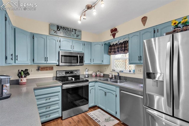 kitchen with blue cabinetry, appliances with stainless steel finishes, sink, and light hardwood / wood-style flooring