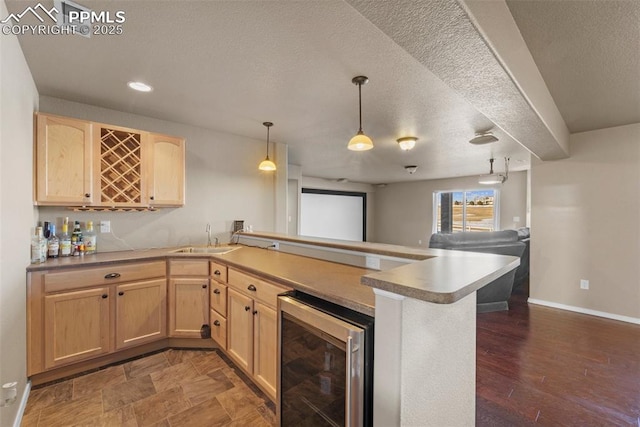 kitchen with light brown cabinetry, sink, kitchen peninsula, pendant lighting, and beverage cooler