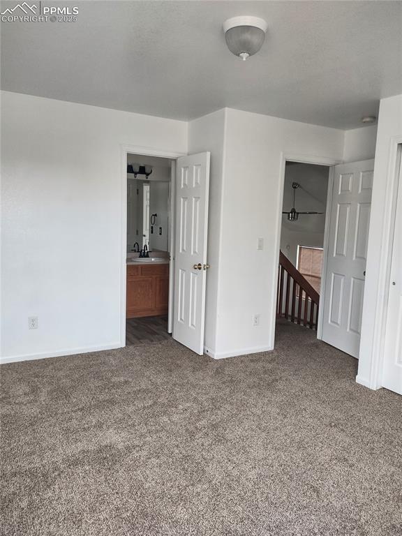 unfurnished bedroom with dark colored carpet, sink, and ensuite bathroom