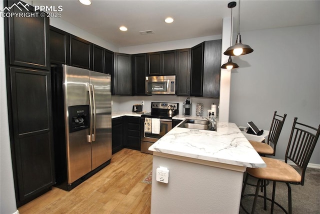 kitchen featuring pendant lighting, sink, stainless steel appliances, a kitchen breakfast bar, and kitchen peninsula