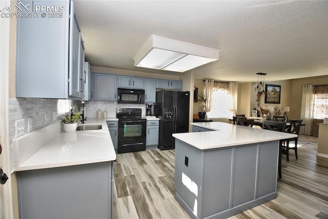 kitchen with pendant lighting, decorative backsplash, light hardwood / wood-style floors, and black appliances