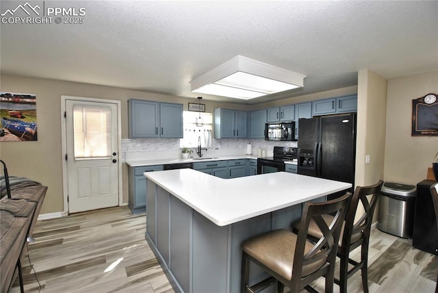 kitchen featuring sink, a kitchen island, black appliances, a kitchen bar, and decorative backsplash