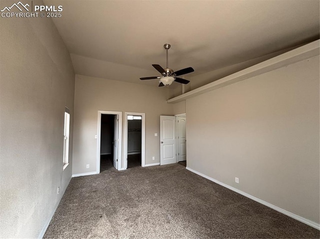 unfurnished bedroom with ceiling fan, a walk in closet, and dark carpet