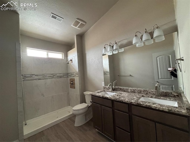 bathroom with wood-type flooring, vanity, tiled shower, toilet, and a textured ceiling