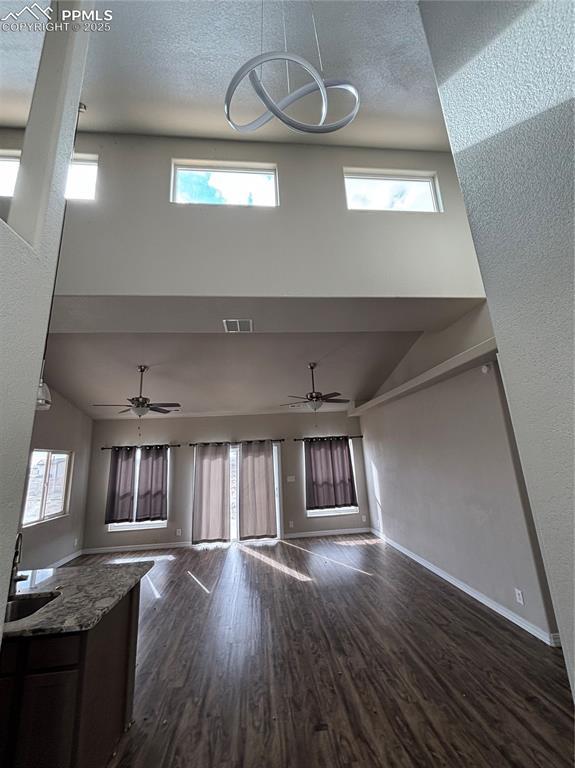 unfurnished living room featuring ceiling fan, plenty of natural light, a towering ceiling, and dark hardwood / wood-style flooring