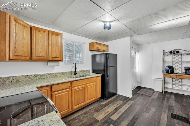 kitchen with sink, black refrigerator, dark hardwood / wood-style floors, light stone counters, and stainless steel range with electric cooktop