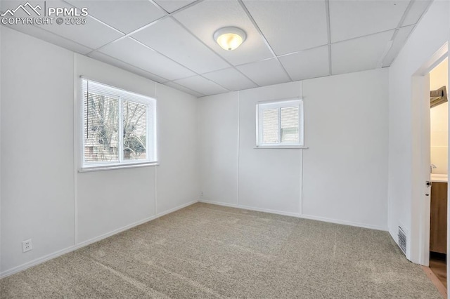 empty room with a drop ceiling, a healthy amount of sunlight, and carpet