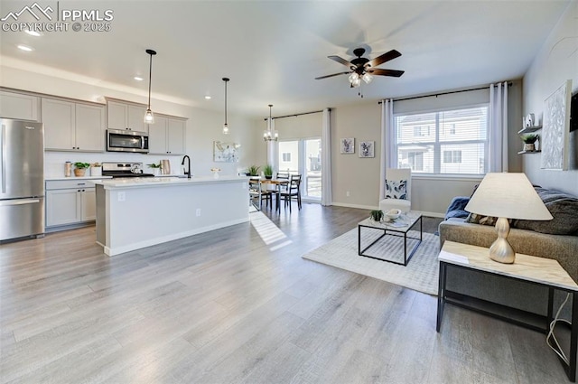 living room with sink, ceiling fan with notable chandelier, a healthy amount of sunlight, and light wood-type flooring