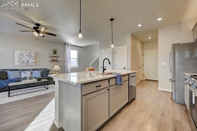 kitchen featuring pendant lighting, sink, appliances with stainless steel finishes, gray cabinetry, and a center island with sink