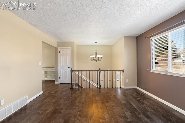 empty room with dark hardwood / wood-style flooring, a textured ceiling, and a notable chandelier