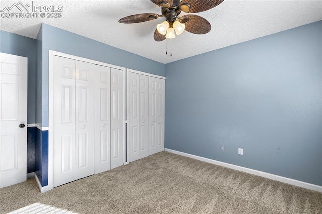 unfurnished bedroom featuring ceiling fan, a textured ceiling, multiple closets, and carpet