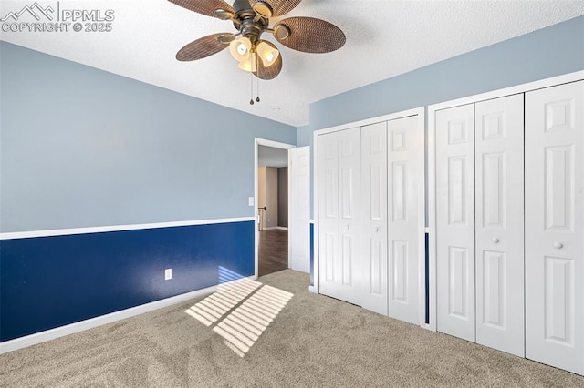 unfurnished bedroom featuring carpet flooring, two closets, a textured ceiling, and ceiling fan