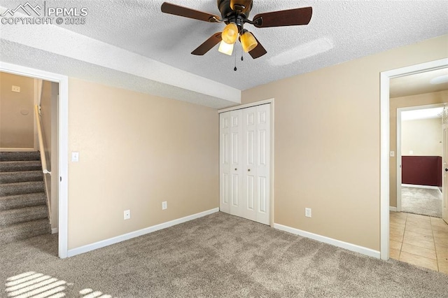 unfurnished bedroom featuring light carpet, ceiling fan, a closet, and a textured ceiling