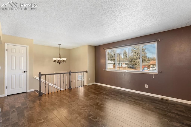 unfurnished room with dark wood-type flooring, an inviting chandelier, and a textured ceiling