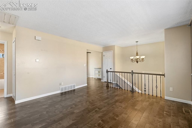 empty room with dark hardwood / wood-style flooring, a textured ceiling, and a notable chandelier