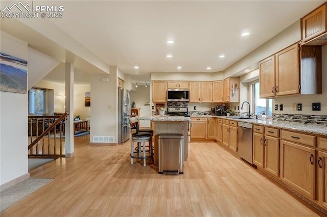 kitchen with a kitchen bar, light stone counters, light wood-type flooring, a kitchen island, and stainless steel appliances