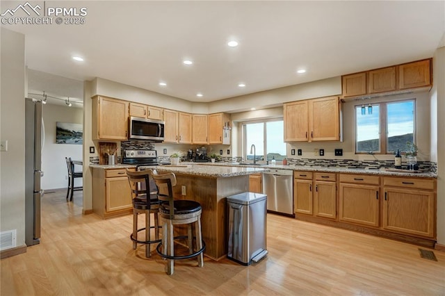 kitchen with sink, light stone counters, appliances with stainless steel finishes, a kitchen breakfast bar, and a kitchen island