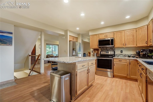 kitchen with light hardwood / wood-style flooring, stainless steel appliances, a center island, light stone countertops, and light brown cabinetry