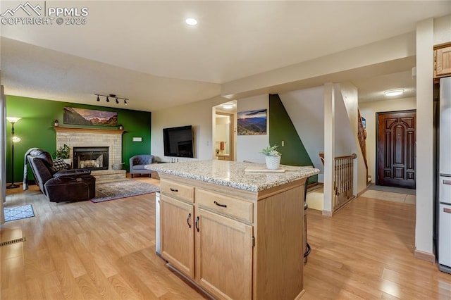 kitchen with light stone counters, light wood-type flooring, light brown cabinets, a kitchen island, and a fireplace