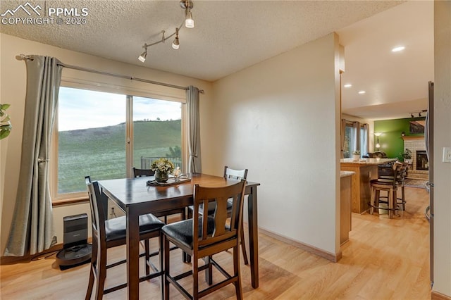 dining space featuring a brick fireplace, light hardwood / wood-style flooring, and a textured ceiling