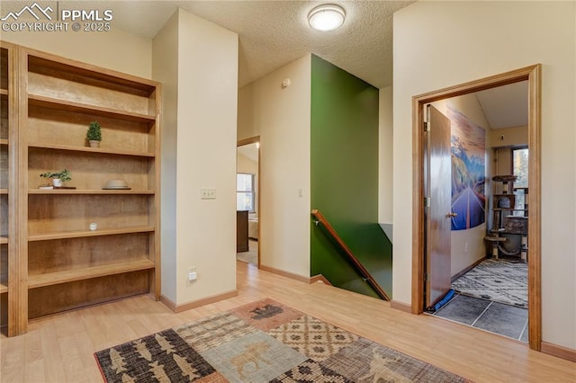 hallway with a textured ceiling and light hardwood / wood-style flooring