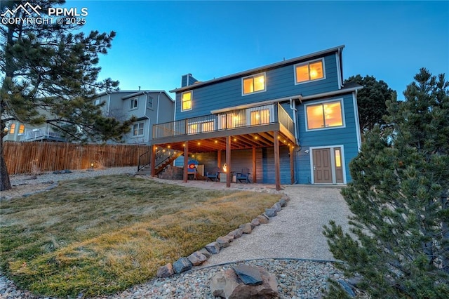 back house at dusk with a wooden deck and a lawn