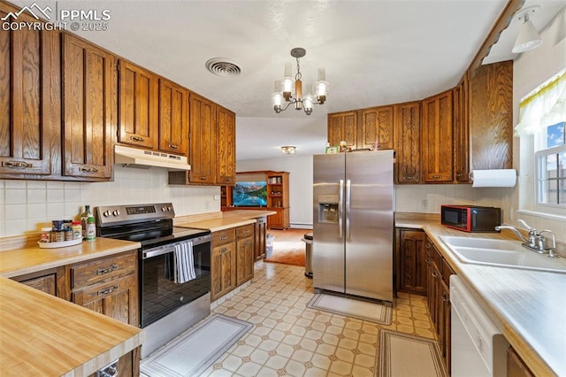 kitchen featuring sink, hanging light fixtures, stainless steel appliances, tasteful backsplash, and a chandelier