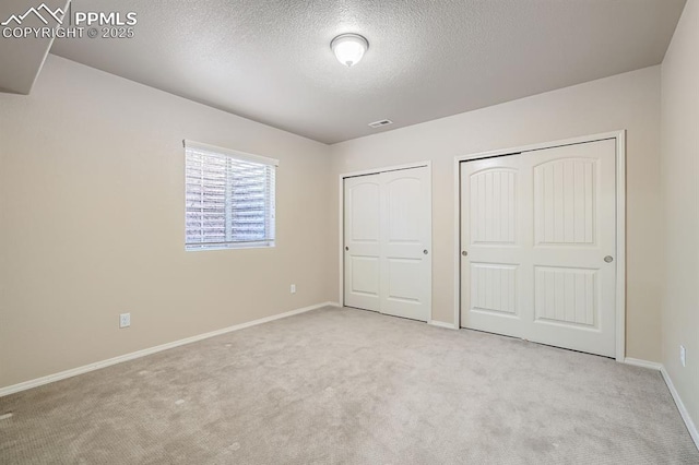 unfurnished bedroom featuring visible vents, baseboards, multiple closets, carpet floors, and a textured ceiling