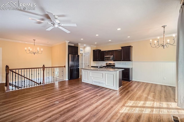 kitchen with a wainscoted wall, visible vents, a kitchen island with sink, light wood-style flooring, and stainless steel appliances