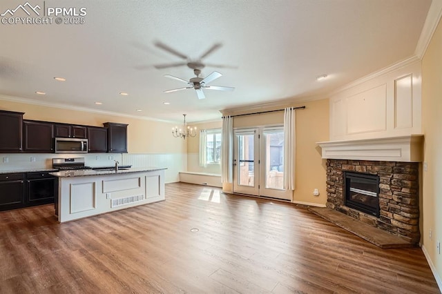 kitchen with wood finished floors, a sink, a stone fireplace, ornamental molding, and stainless steel appliances