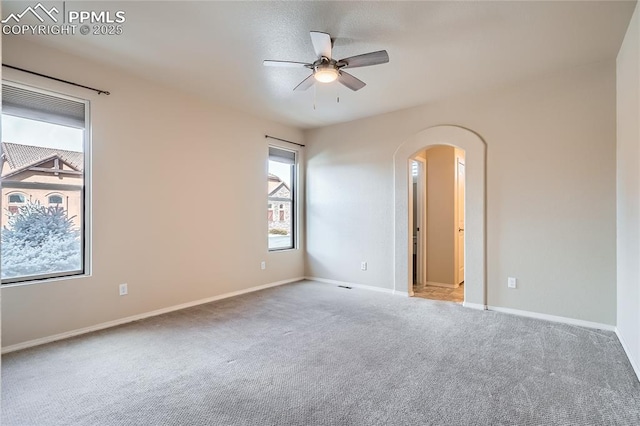 empty room featuring baseboards, carpet, arched walkways, and ceiling fan