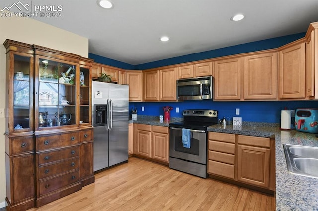 kitchen with dark stone countertops, sink, stainless steel appliances, and light wood-type flooring