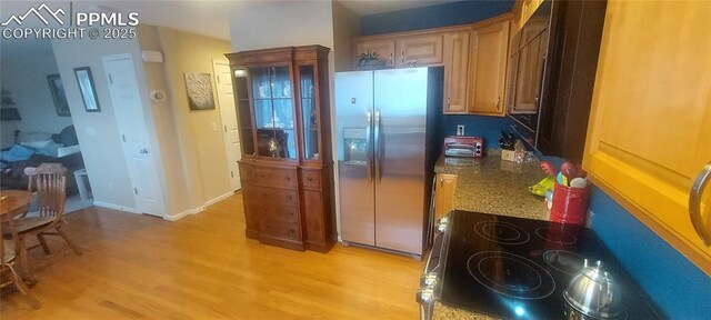 kitchen featuring stainless steel refrigerator with ice dispenser, dark stone countertops, and light wood-type flooring