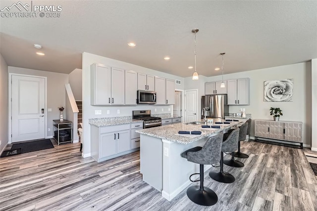 kitchen with appliances with stainless steel finishes, pendant lighting, a breakfast bar area, a kitchen island with sink, and light stone countertops