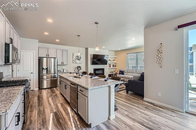 kitchen with sink, light stone counters, decorative light fixtures, stainless steel appliances, and a kitchen island with sink