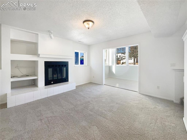 unfurnished living room featuring carpet floors, a tile fireplace, and a textured ceiling