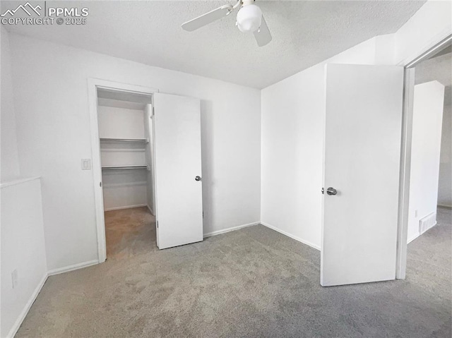 unfurnished bedroom featuring light carpet, ceiling fan, a spacious closet, and a textured ceiling