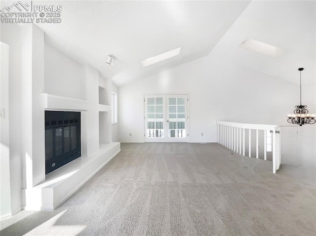 unfurnished living room featuring light carpet, lofted ceiling with skylight, french doors, and a chandelier