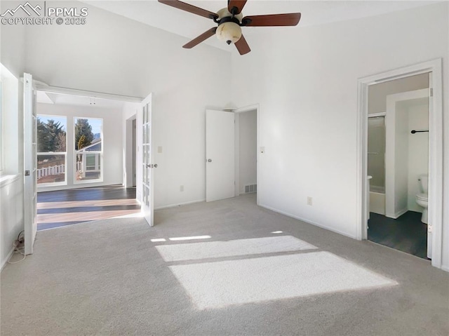 unfurnished bedroom featuring light carpet, connected bathroom, a towering ceiling, and ceiling fan