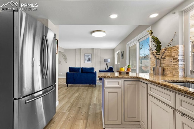 kitchen featuring stainless steel refrigerator, light stone countertops, kitchen peninsula, cream cabinets, and light hardwood / wood-style flooring