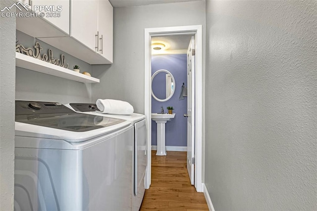 washroom with cabinets, sink, independent washer and dryer, and light hardwood / wood-style flooring