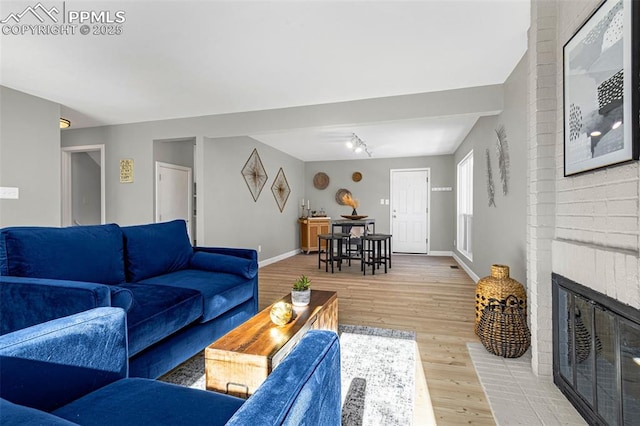 living room featuring track lighting, a brick fireplace, and light wood-type flooring