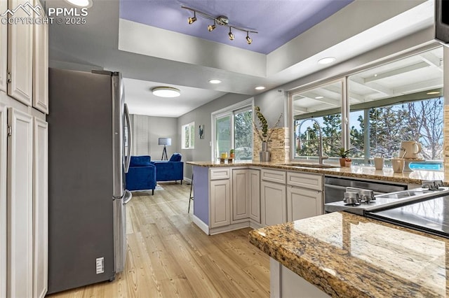 kitchen with light stone counters, sink, stainless steel fridge, and light wood-type flooring