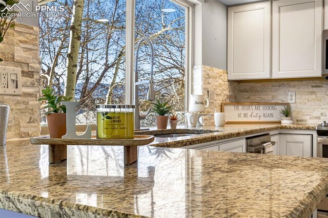 kitchen with white cabinetry, sink, light stone counters, and backsplash