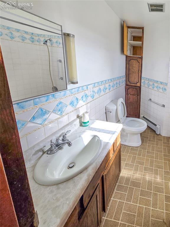 bathroom featuring tile walls, a baseboard heating unit, vanity, toilet, and walk in shower