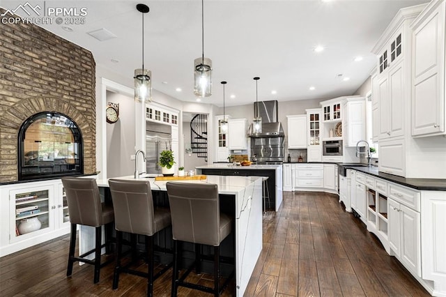 kitchen featuring sink, hanging light fixtures, an island with sink, white cabinets, and wall chimney exhaust hood