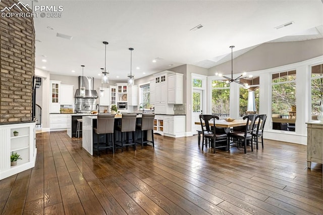 kitchen with a spacious island, wall chimney exhaust hood, a breakfast bar area, decorative light fixtures, and dark hardwood / wood-style floors