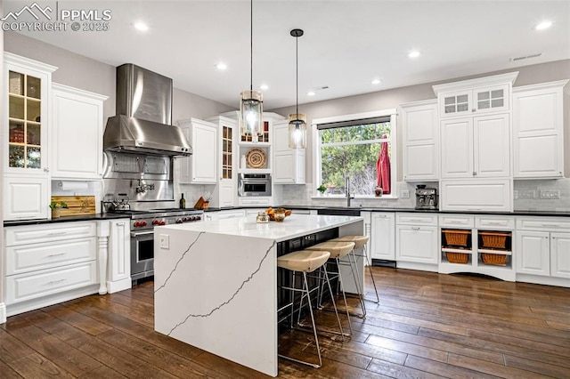 kitchen featuring a kitchen island, decorative light fixtures, white cabinets, stainless steel appliances, and wall chimney range hood