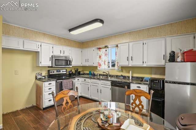 kitchen featuring appliances with stainless steel finishes, dark hardwood / wood-style floors, sink, dark stone countertops, and white cabinets